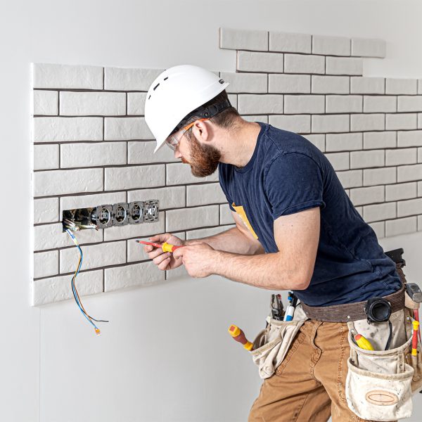 Electrician construction worker with a beard in overalls during the installation of sockets. Home renovation concept.