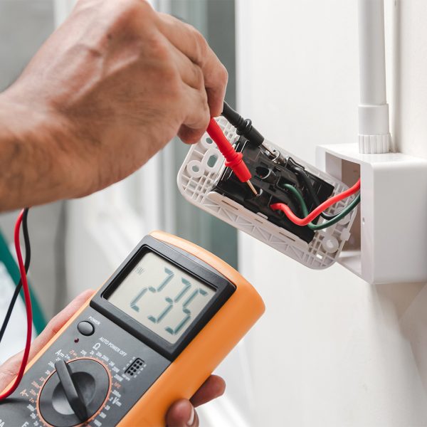 Electrician is using a digital meter to measure the voltage at the power outlet in on the wall.