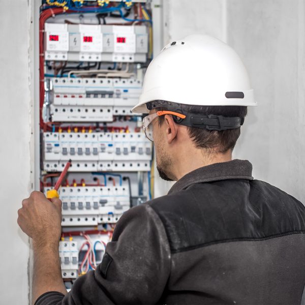 Man, an electrical technician working in a switchboard with fuses. Installation and connection of electrical equipment. Professional with tools in hand. concept of complex work, space for text.